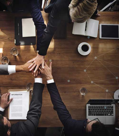 Top view of a wooden conference table with six professionals stacking hands.